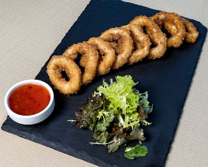 Fried calamari rings served on a slate platter with dipping sauce and mixed greens, highlighting peasant food affordability.