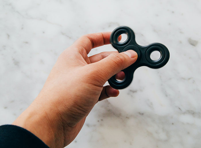 Hand holding a black fidget spinner on a marble surface representing big trends almost forgotten.