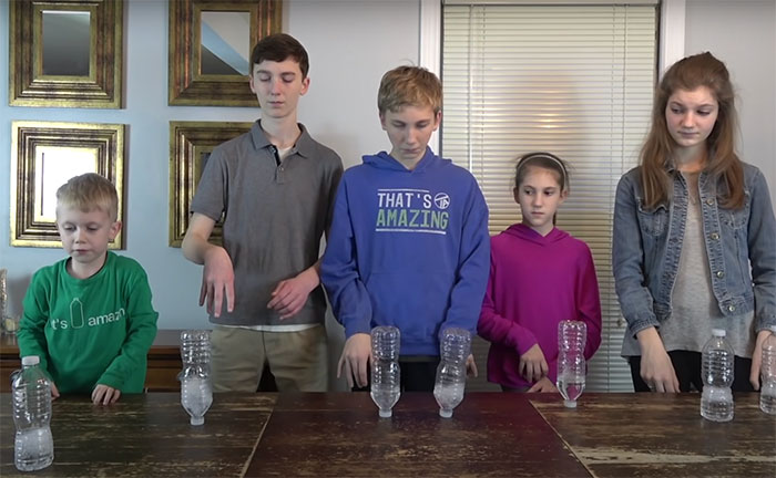 Five kids lined up at a table, performing a cup stacking activity showcasing popular big trends from the past.