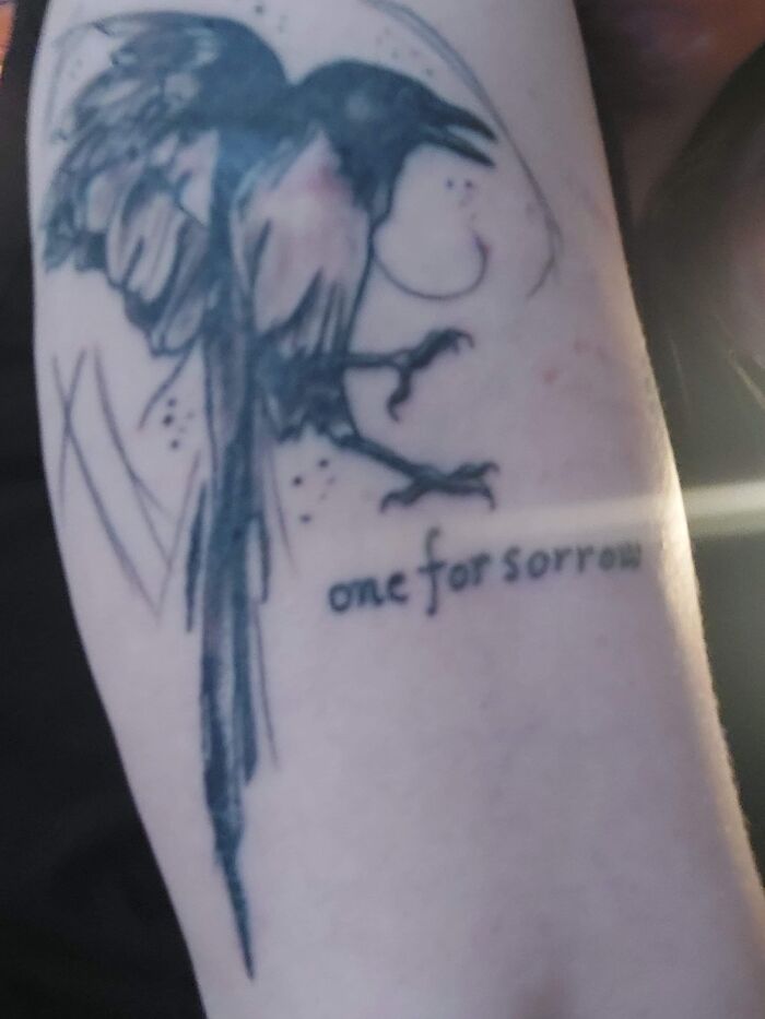Tattoo of a magpie with the words "one for sorrow" on an arm.