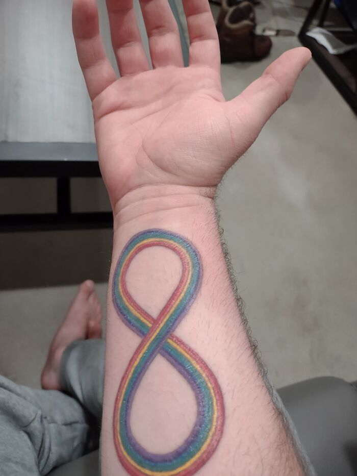 Tattoo of a colorful infinity symbol on a forearm.