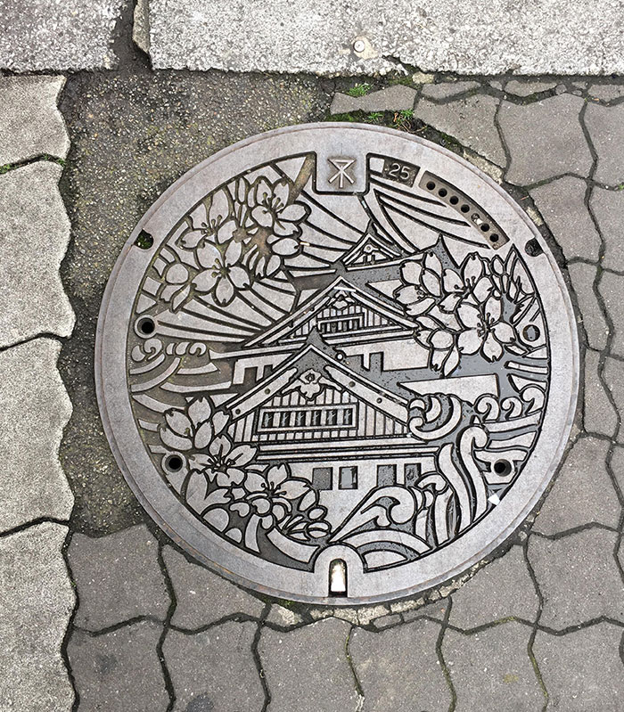 Decorative Japanese manhole cover featuring traditional architecture and cherry blossoms, highlighting unique Japanese inventions.