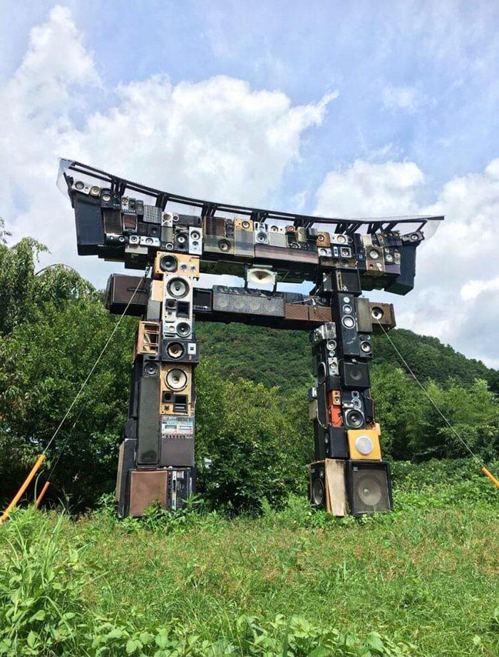 Large outdoor sculpture resembling a traditional Japanese torii gate made from stacked vintage speakers and audio equipment.