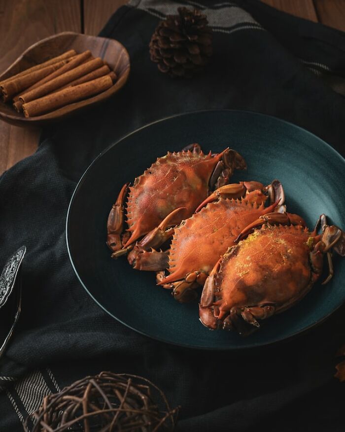 Three cooked crabs on a dark plate, illustrating seafood products people can no longer afford due to rising costs.