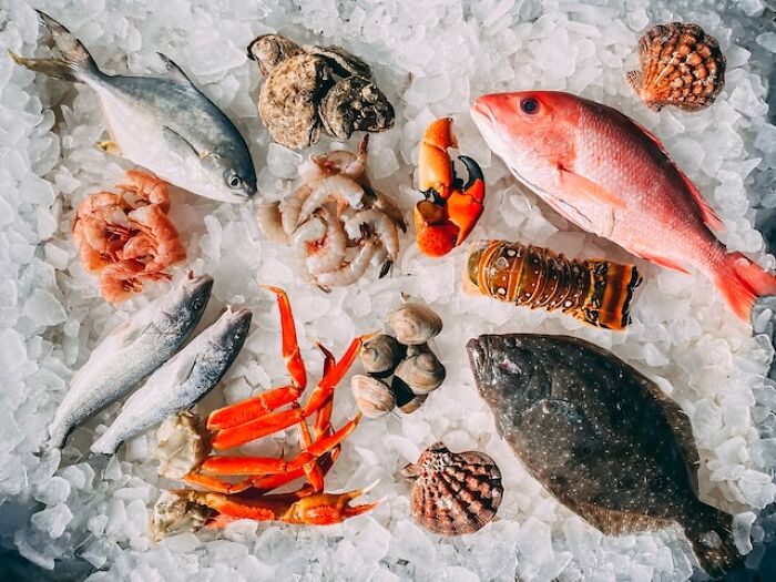 Various types of seafood including fish, crab legs, shrimp, and shellfish displayed on crushed ice, highlighting price impact.
