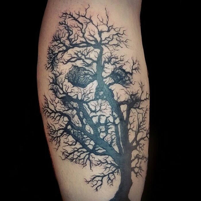 Optical illusion tattoo of a tree forming a skull on a person's arm.