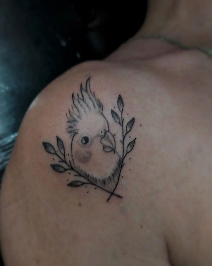Pet tattoo of a cockatiel with leaves on a person's shoulder, showcasing an adorable design.