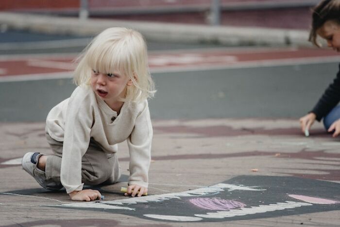 Child drawing with chalk on pavement outdoors, illustrating themes related to bad parenting and honest thoughts shared.