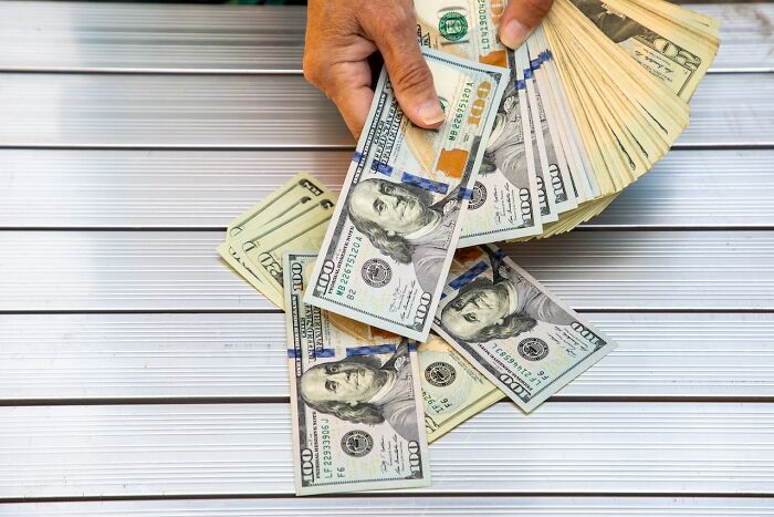 Hands holding a large stack of US hundred dollar bills representing unexpected outcomes of good intentions.