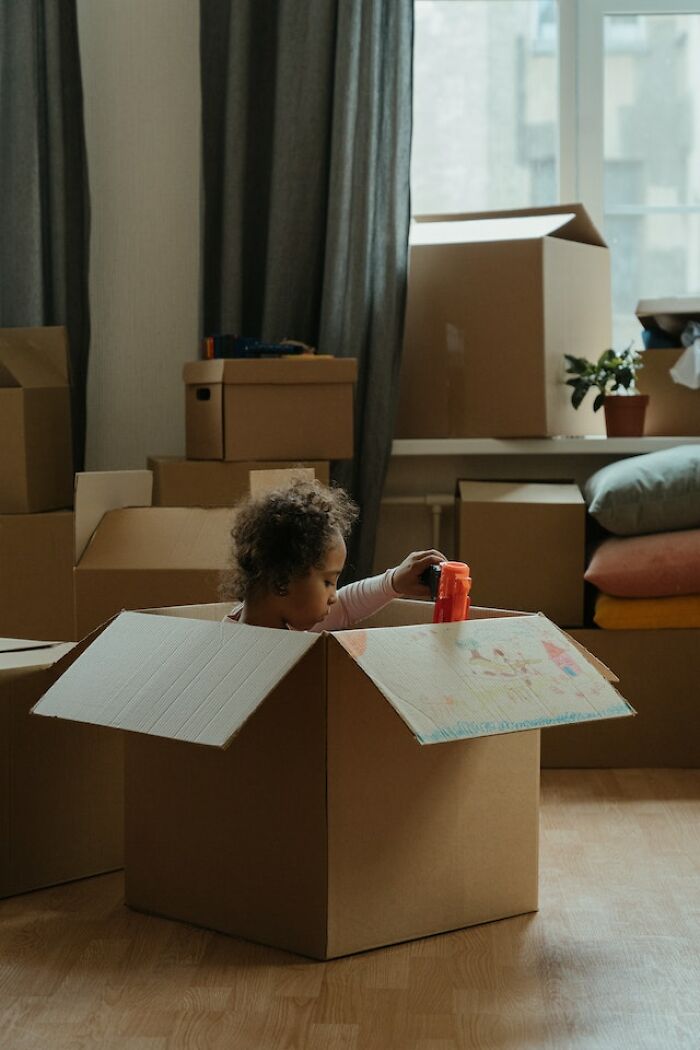 Child playing inside a cardboard box surrounded by unpacked boxes, reflecting on what screams bad parenting.