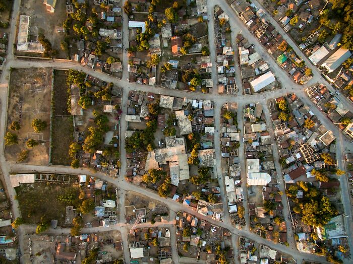 Aerial view of a dense neighborhood with intersecting roads and scattered trees at sunset, symbolizing unintended consequences.