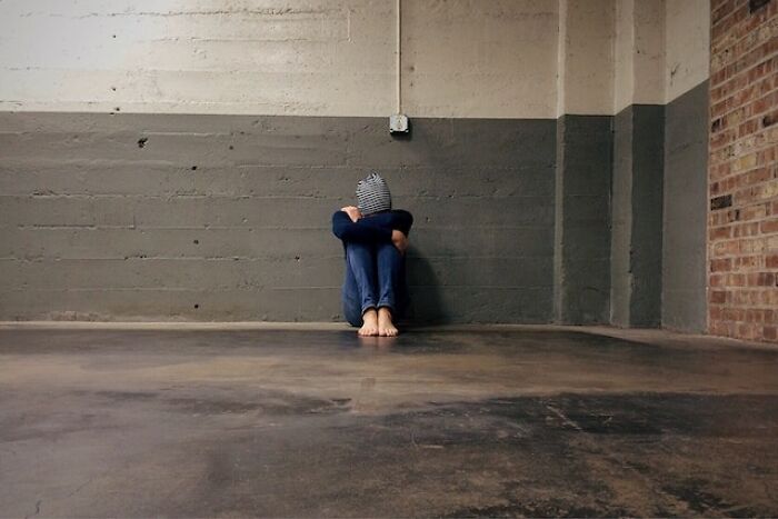 Person sitting alone on a concrete floor against a wall, representing feelings related to being a bad parent.