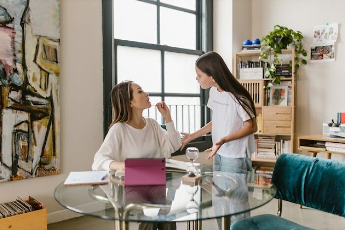 Woman and teenage daughter having a tense conversation about parenting in a modern living room setting.