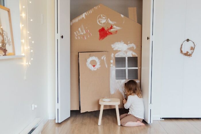 Child sitting on floor painting cardboard house inside home, illustrating what screams bad parent in honest thoughts discussion.