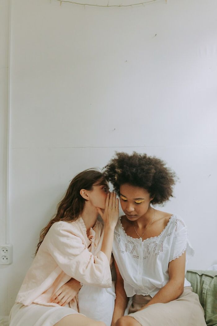 Two women sitting close as one whispers into the other's ear, reflecting honest thoughts on bad parent concerns.