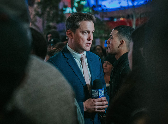 News reporter in a blue suit holding a microphone, covering a story about professions that may soon disappear.