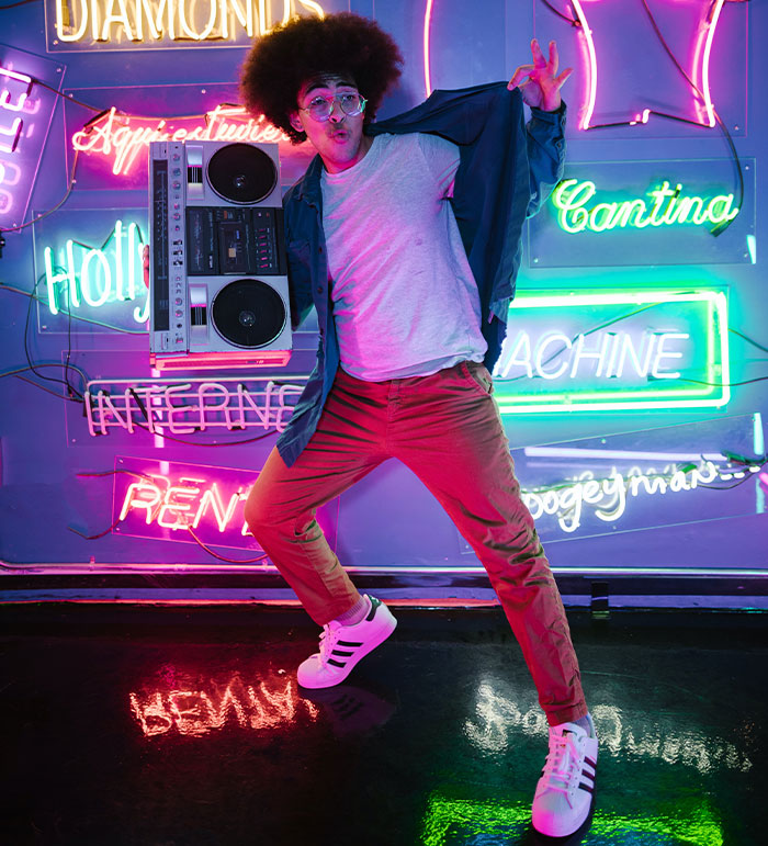 Man with afro and glasses holding boombox posing in colorful neon-lit room, reflecting professions that may soon disappear