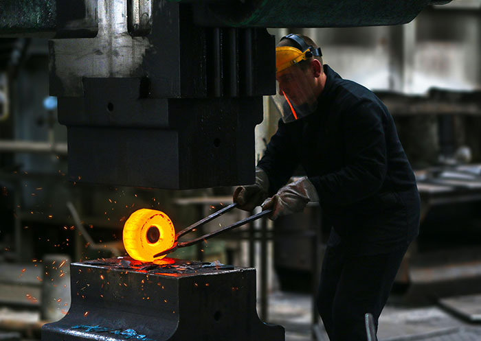 Blacksmith forging glowing hot metal using an industrial machine, representing professions that may soon disappear.
