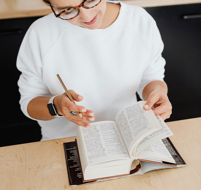 Woman wearing glasses and a white sweatshirt reading a book and taking notes about professions that may soon disappear.
