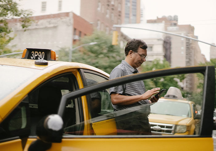 Taxi driver standing near car door in a city, illustrating one of the professions that may soon disappear.