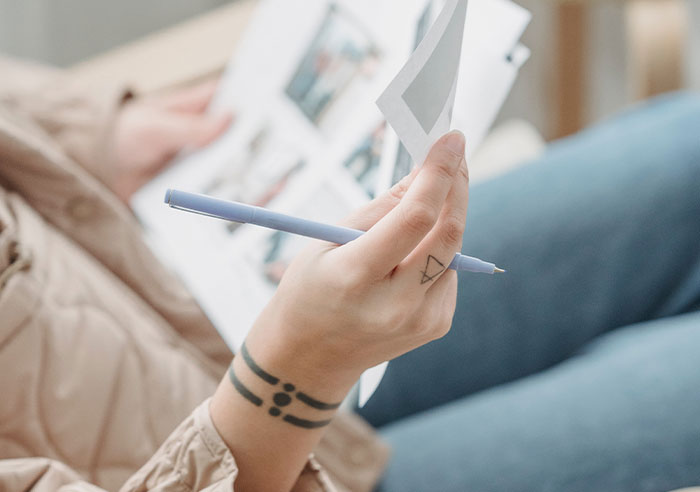Person with tattoos holding a pen and reviewing photos, symbolizing professions that may soon disappear.