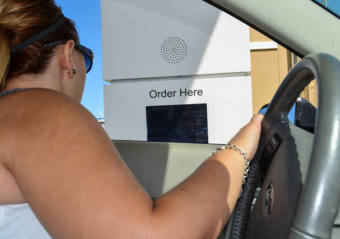 Woman in car using a fast food drive-thru speaker, illustrating professions that may soon disappear concept.
