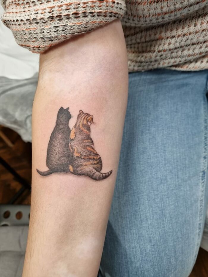 Tattoo of two cats sitting together on a person's forearm, symbolizing pet companionship.