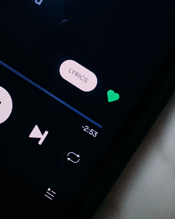 Close-up of a phone screen showing a music player interface with lyrics and a green heart icon during texting games.