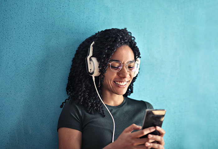 Young woman with headphones smiling while using phone, enjoying texting games during a casual conversation session.