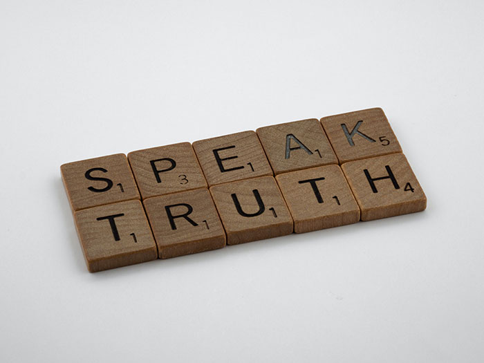 Wooden letter tiles arranged to spell speak truth, illustrating texting games for phone conversations.