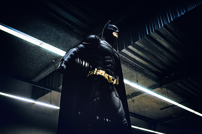Batman costume with cape and utility belt standing in a dark industrial setting illustrating texting games concept.