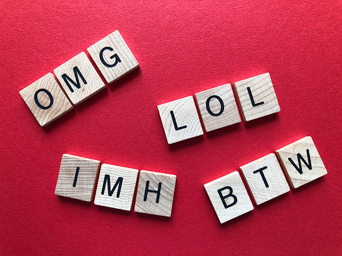 Wooden letter tiles on a red background spelling out common texting abbreviations for texting games and conversations.