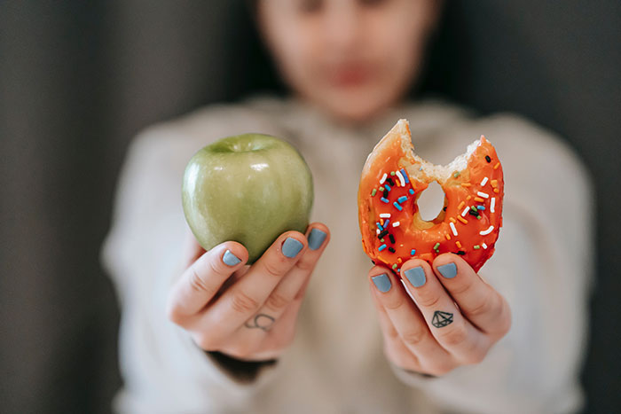 Person holding a green apple in one hand and a bitten donut with sprinkles in the other, texting games concept.