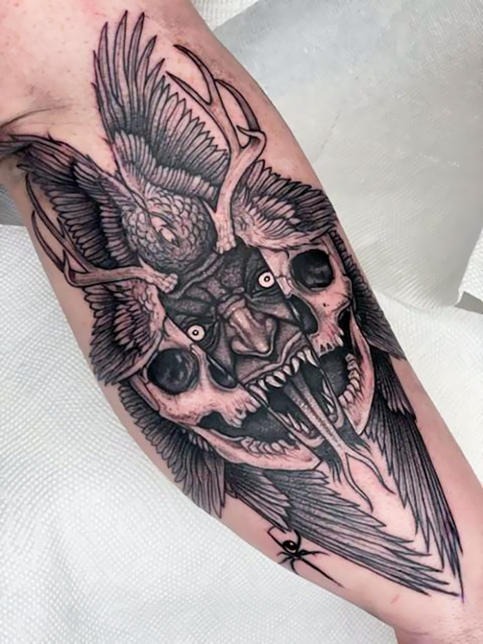 Detailed trippy tattoo featuring a skull, bird, and antlers on forearm.