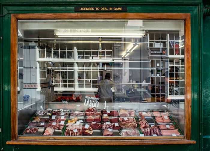 Butcher shop window with various fresh meat cuts, highlighting products some people can no longer afford.