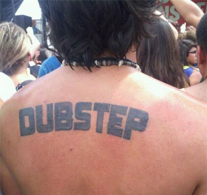 Back tattoo with "DUBSTEP" in bold letters at an outdoor event, representing a cringe-worthy tattoo style.