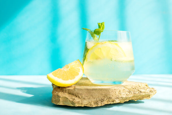 A refreshing lemon drink with mint on a stone slab, set against a bright blue background.