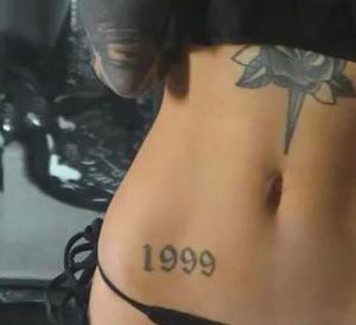 "Lower back tattoo of the year 1999 with a decorative design above on bare skin."