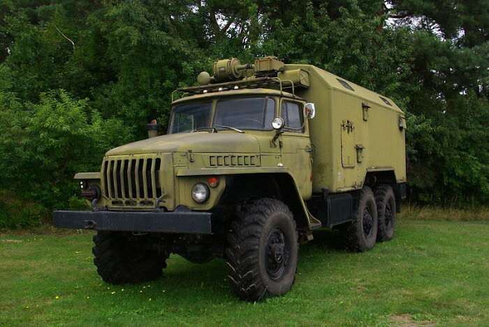 Large military truck parked on grass near trees, symbolizing the road to hell paved with good intentions concept.