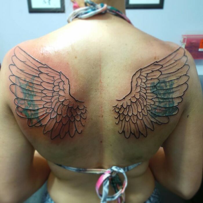 Wings tattoo on a person's back in progress, showing detailed outlines and light shading.