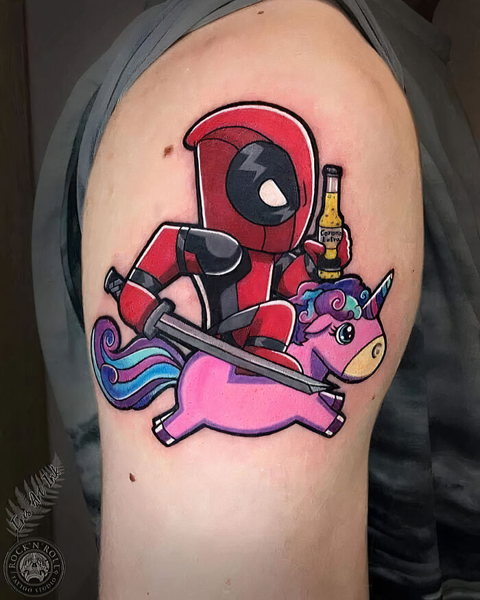 Funny tattoo of a cartoon character riding a pink unicorn and holding a beverage.