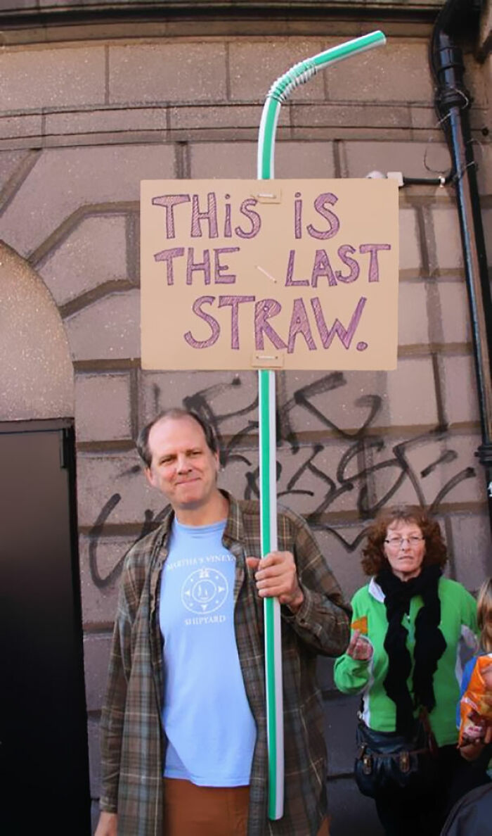 Man holding a humorous protest sign with a giant straw saying this is the last straw in a public setting.