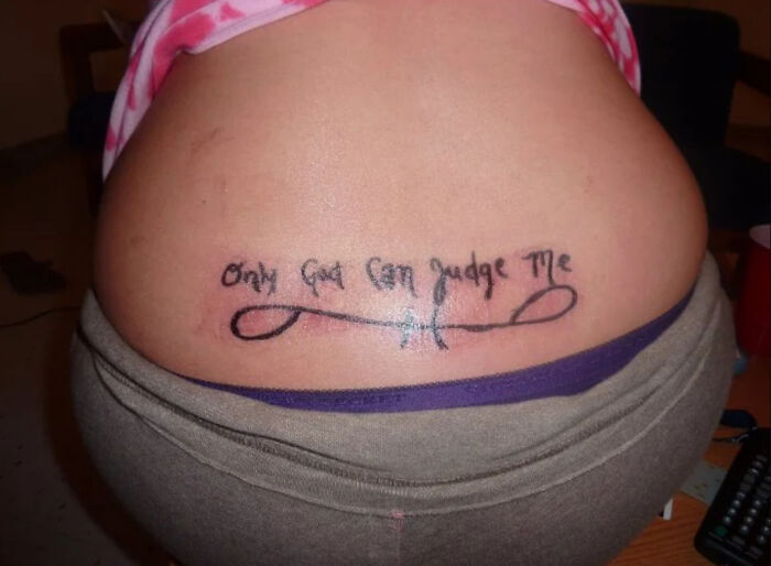 Lower back tattoo with text "Only God Can Judge Me," featuring intricate line design.