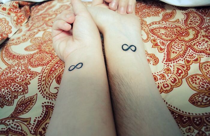 Matching infinity symbol tattoos on wrists against a patterned background.