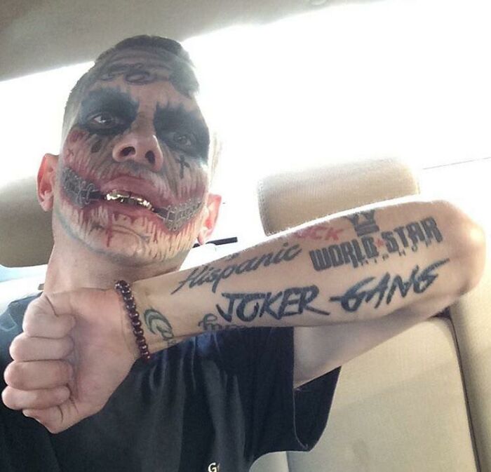 Person with face paint and tattooed forearm, showing the tattoo and wearing a black shirt.