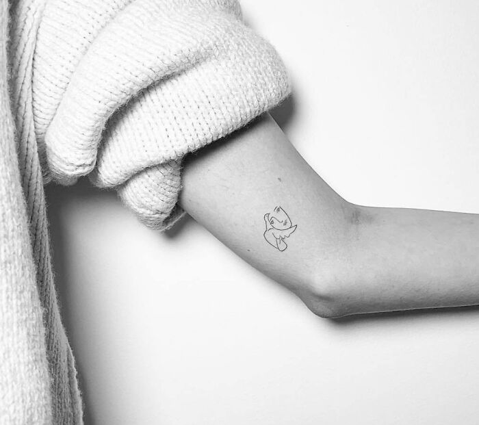 Celebrity tattoo of cartoon character on inner arm, person wearing a knitted sweater.