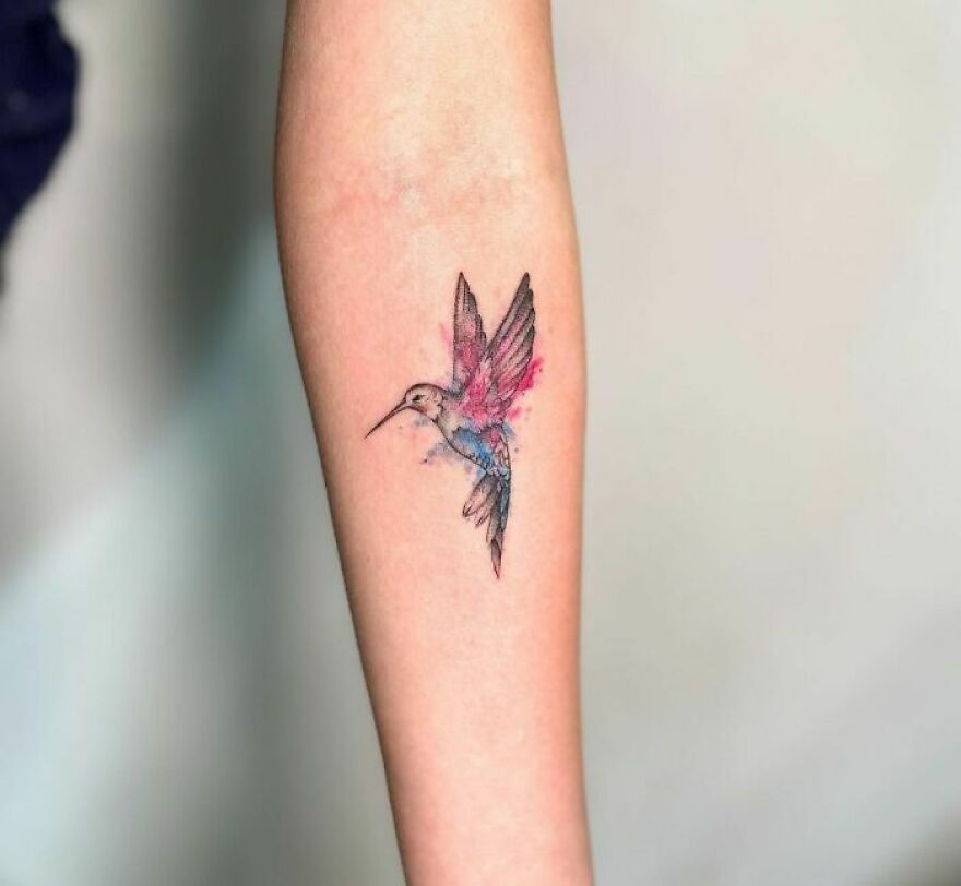 Watercolor tattoo of a hummingbird on a forearm, showcasing vibrant colors and delicate details.