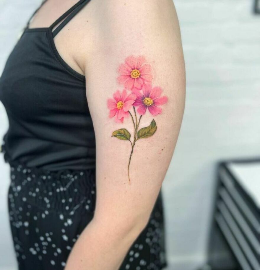 Pink floral watercolor tattoo on upper arm, showcasing delicate flowers and leaves.