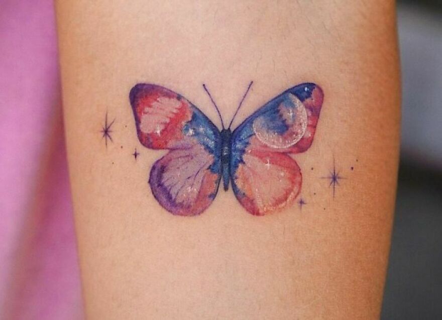 Watercolor butterfly tattoo with vibrant pink, purple, and blue hues on skin.