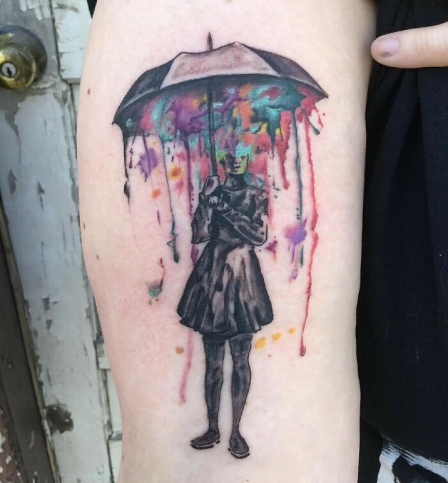 Watercolor tattoo of a person under an umbrella with colorful paint drips forming a vibrant background.